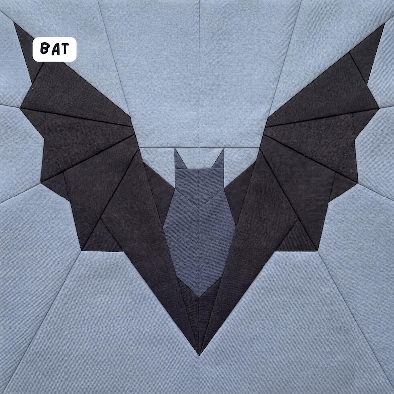 May include: A geometric quilt block featuring a bat design. The bat is depicted with dark gray wings and a lighter gray body, set against a light blue background. The word "BAT" is in a white box in the upper left corner.