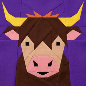 Puede incluir: Un bloque de edredón geométrico que representa la cabeza estilizada de un toro. El toro tiene pelaje marrón, hocico rosa claro y cuernos amarillos. El fondo es de color morado liso y el diseño está hecho de piezas de tela.