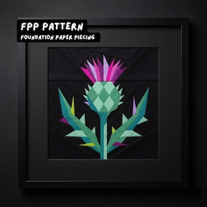 May include: Framed artwork featuring a geometric thistle design. The thistle is rendered in shades of green, purple, and pink against a black background. The artwork is framed in a black square frame. Text at the top reads "FPP PATTERN" and "FOUNDATION PAPER PIECING".