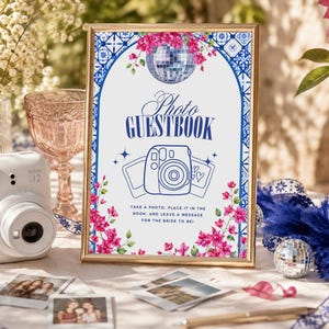 May include: A gold-framed sign featuring a blue and white tile pattern border, pink bougainvillea flowers, a disco ball, and a blue line-art camera illustration. The text reads: Photo GUESTBOOK. Take a photo, place it in the book, and leave a message for the bride to be!
