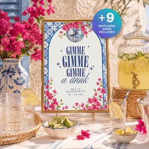 Könnte beinhalten: Ein rechteckiges Schild in einem goldenen Rahmen mit blau-weißem Fliesenmuster, rosa Bougainvillea-Blüten, einer Discokugel und dem Text GIMME GIMME GIMME a drink EMILY'S BACHELORETTE 26 - 28 AUG sowie einem blauen Kreis mit der Aufschrift +9 MATCHING SIGNS INCLUDED.