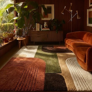 Può includere: Un moderno tappeto con un design geometrico nei toni del ruggine, verde oliva, beige e bianco. Il tappeto presenta forme curve e rettangolari, aggiungendo un tocco contemporaneo all'arredamento della stanza. Il tappeto è in un soggiorno.
