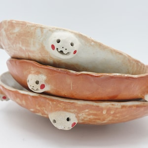 May include: A stack of three ceramic bowls with a brown glaze. Each bowl has a small, white face with red cheeks on the side.