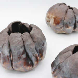 May include: Three ceramic pots with a textured, uneven surface. The pots are brown and gray with a slightly metallic sheen. The pots are all different sizes and shapes.