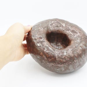 Könnte beinhalten: Eine braune Keramikschale mit einer strukturierten Oberfläche und einer runden Öffnung in der Mitte. Die Schale hat eine gesprenkelte Optik mit weißen und braunen Flecken.