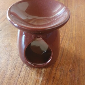 Może przedstawiać: Brązowy ceramiczny dyfuzor olejków eterycznych z okrągłym naczyniem na górze i otworem w kształcie łzy z przodu. Dyfuzor stoi na drewnianej powierzchni. Naczynie jest przeznaczone do przechowywania olejków eterycznych.