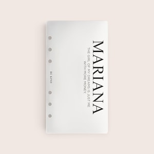 Pode incluir: Um inserto de planejador branco com o nome "MARIANA" em fonte serif preta grande. O texto "THE GIRL OF MY DREAMS IS JUST ME WITH MORE MONEY" está abaixo. As palavras "BE KIND" são impressas verticalmente.