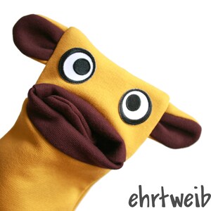 May include: A yellow hand puppet with brown ears and large black eyes. The puppet's mouth is open and has a brown lining.