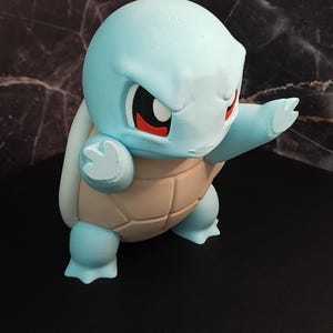 May include: A light blue Squirtle figure with a tan shell, red eyes, and a determined expression. The figure is posed with one arm raised. The figurine is a collectible item.