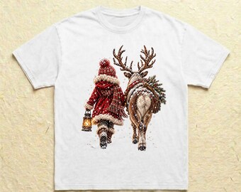 Könnte beinhalten: Ein weißes Kurzarm-T-Shirt mit einem Grafikdruck einer Figur in rotem Wintermantel und Mütze, die eine leuchtende Laterne hält und neben einem Rentier mit großem Geweih und einem kleinen Tannenbaum auf dem Rücken geht.