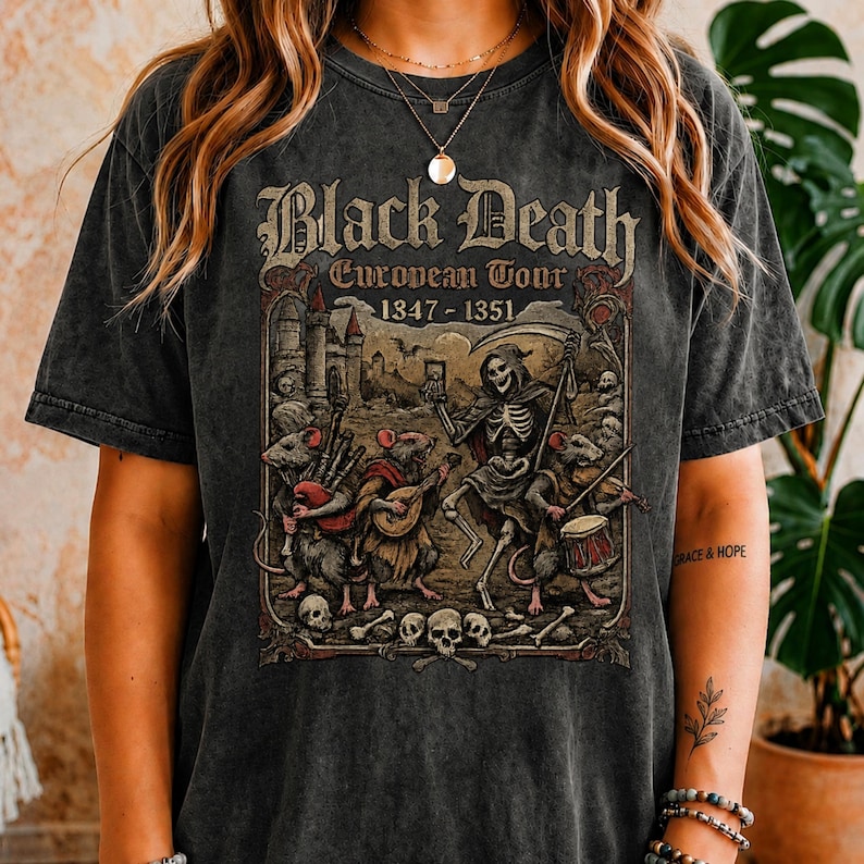 May include: Dark gray t-shirt featuring a vintage-style graphic for the "Black Death European Tour 1347-1351." The design includes a skeleton with a scythe, rats, skulls, and musical instruments. The shirt has a distressed look.
