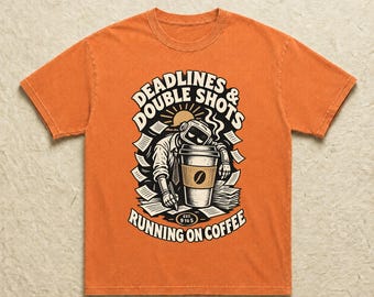 Könnte beinhalten: Ein orangefarbenes T-Shirt mit einem Grafikdruck, der einen Roboterkopf zeigt, der auf einem großen Kaffeebecher ruht, umgeben von verstreuten Papieren. Der Text lautet DEADLINES & DOUBLE SHOTS und RUNNING ON COFFEE mit EST. 9 TO 5 in Schwarz und Weiß.