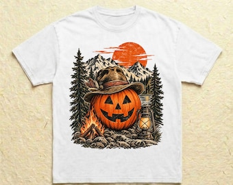 Könnte beinhalten: Ein weißes T-Shirt mit einem Grafikdruck eines Halloween-Kürbisses, der einen braunen Fedora-Hut trägt. Die Szene zeigt ein Lagerfeuer, eine alte Laterne, hohe Kiefern und schneebedeckte Berge unter einer großen orangefarbenen Sonne.