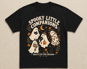 Könnte beinhalten: Ein schwarzes Kurzarm-T-Shirt mit einem Grafikdruck mit dem Text "SPOOKY LITTLE COMPANIONS" und "HAUNTING THE SEASON". Das Design zeigt drei weiße Geister, schwarze Katzen, einen Kürbis und herbstliche Blätter.