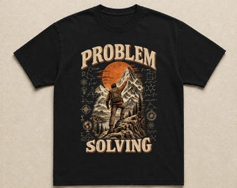 Könnte beinhalten: Ein schwarzes Kurzarm-T-Shirt mit einem Grafikdruck eines Wanderers, der auf einem felsigen Gipfel steht und auf eine große orangefarbene Sonne zeigt. Das Design enthält den Text PROBLEM SOLVING und verschiedene mathematische Symbole.