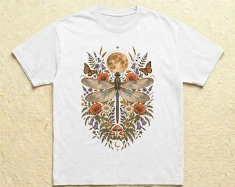 Könnte beinhalten: Ein weißes T-Shirt mit kurzen Ärmeln und einer zentralen Grafikillustration einer großen Libelle unter einem Vollmond, umgeben von orangefarbenen Mohnblumen, weißen Gänseblümchen, violetten Glockenblumen, Farnen, Pilzen und zwei Monarchfaltern.