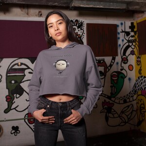 May include: A gray cropped hoodie with the text "PRIVATE MODE" and a graphic of a face wearing headphones. The person is wearing black jeans. The background is a graffiti-covered wall.