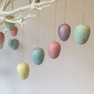 Peut inclure: Une branche blanche avec des œufs de Pâques mouchetés de couleur pastel suspendus. Les œufs sont dans des tons de rose, bleu, vert et jaune.