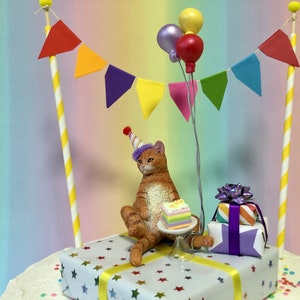 May include: Orange tabby cat wearing a purple and white party hat sitting on a white gift box with yellow ribbon and blue stars. The cat is holding a slice of rainbow cake. There are two yellow and white striped poles with red, orange, purple, yellow, pink, green and blue triangle flags. There are three balloons: one silver, one pink and one red.