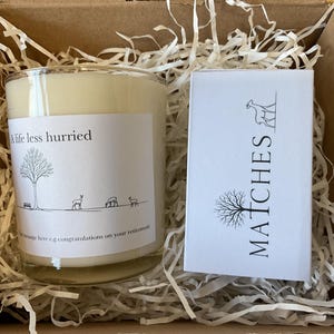 Puede incluir: Un juego de regalo en una caja de cart&oacute;n, que contiene una vela de vidrio con el texto "A life less hurried" y una peque&ntilde;a caja blanca de cerillas. La vela tiene una etiqueta con una ilustraci&oacute;n de un &aacute;rbol y ciervos. La caja de cerillas dice "MATCHES".