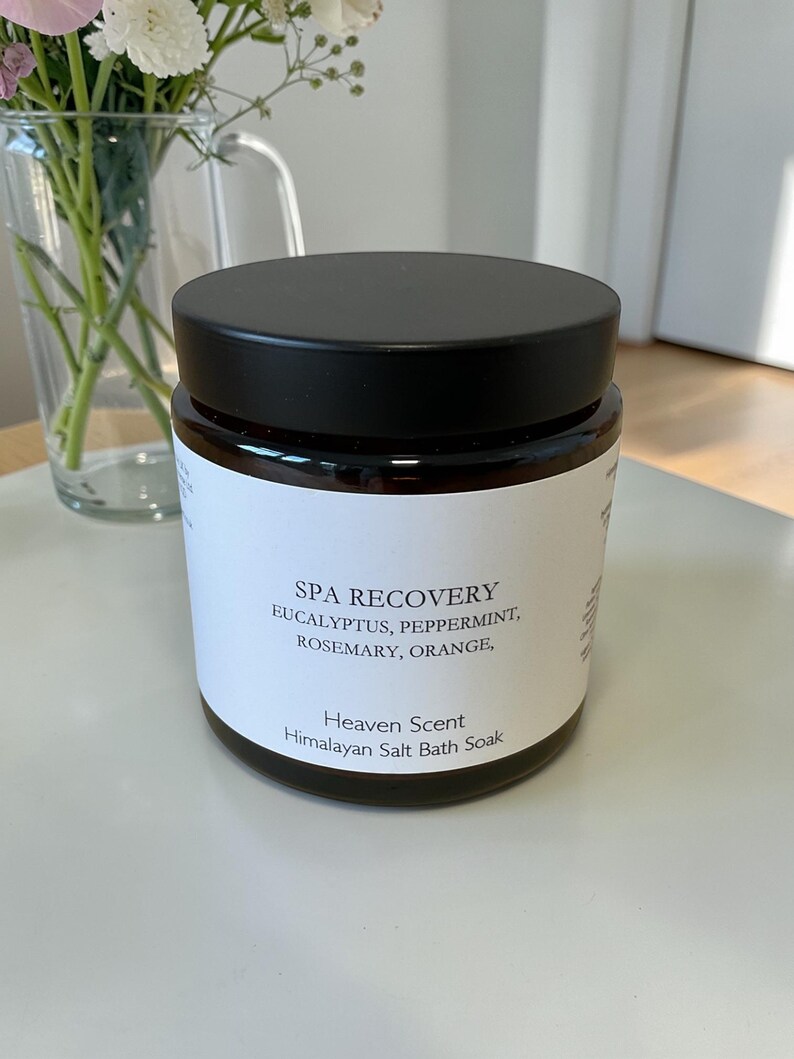 Puede incluir: Un tarro de vidrio oscuro con tapa negra y etiqueta blanca. La etiqueta dice "SPA RECOVERY" con los ingredientes: eucalipto, menta, romero y naranja. Es una sal de ba&ntilde;o del Himalaya de Heaven Scent.