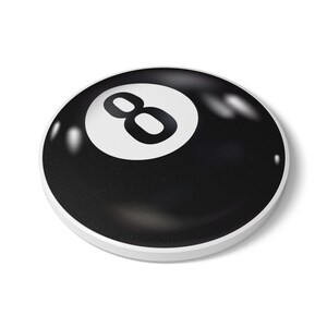 May include: A circular, black button featuring a white center circle with the black number eight printed in the middle. The surface has a smooth, glossy finish with visible light reflections, and the edge is bordered by a thin white rim.