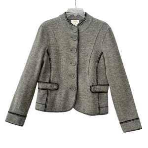 May include: A grey jacket featuring a stand-up collar, long sleeves, and a front button closure. The garment is accented with black decorative stitching along the seams, cuffs, and two horizontal front pockets, each finished with a single button.