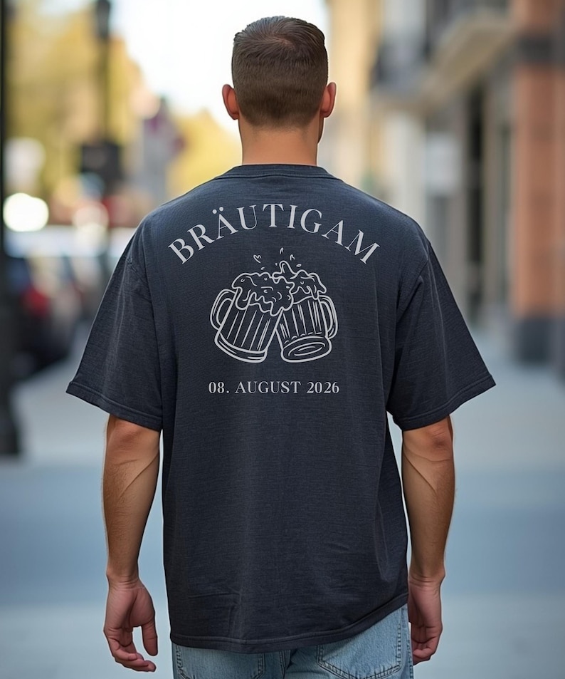 K&ouml;nnte beinhalten: Ein dunkelgraues T-Shirt mit kurzen &Auml;rmeln und einer wei&szlig;en Strichgrafik auf der R&uuml;ckseite. Das Motiv zeigt zwei ansto&szlig;ende Bierkr&uuml;ge mit Schaum, dar&uuml;ber der Text BR&Auml;UTIGAM und darunter das Datum 08. AUGUST 2026 in wei&szlig;er Schrift.