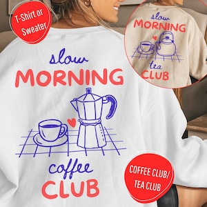 Könnte beinhalten: Ein weißes Sweatshirt mit einer blau-roten Grafik, die eine Mokkakanne, eine Kaffeetasse auf einer Untertasse und ein kleines Herz zeigt. Der Text lautet slow MORNING coffee CLUB. Ein Einschub zeigt eine beige Version mit einer Teekanne und dem Text slow MORNING tea CLUB.