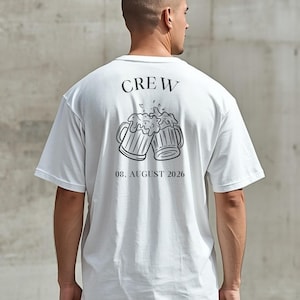 K&ouml;nnte beinhalten: Ein wei&szlig;es kurz&auml;rmeliges T-Shirt mit einer schwarzen Grafik auf der R&uuml;ckseite. Das Design zeigt das Wort CREW &uuml;ber zwei ansto&szlig;enden Bierkr&uuml;gen mit Schaum sowie den Text 08. AUGUST 2026 in schwarzer Schrift unter der Abbildung.