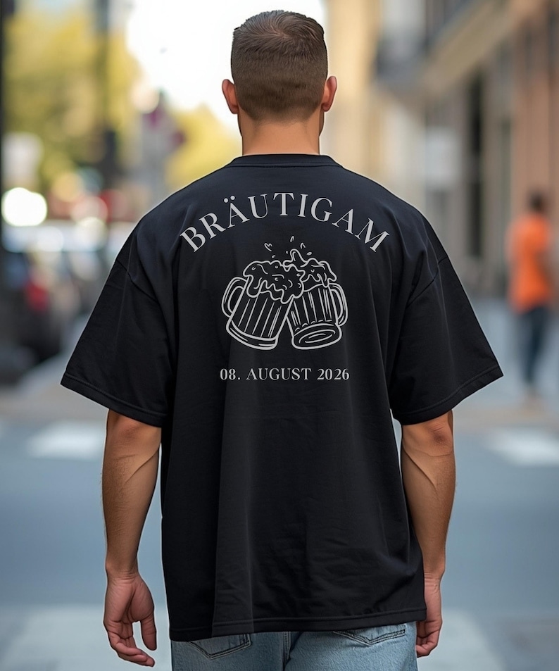 K&ouml;nnte beinhalten: Ein schwarzes Kurzarm-T-Shirt mit einer wei&szlig;en Strichzeichnung von zwei ansto&szlig;enden Bierkr&uuml;gen auf der R&uuml;ckseite. &Uuml;ber den Kr&uuml;gen steht der Text BR&Auml;UTIGAM in Serifenschrift, darunter das Datum 08. AUGUST 2026 in passender wei&szlig;er Schrift.