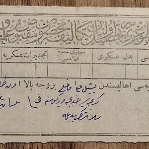 May include: A rectangular, off-white paper document featuring printed grid lines and handwritten text in Ottoman Turkish script. The document includes a circular stamped seal in the bottom left corner and various numerical entries within the table structure.