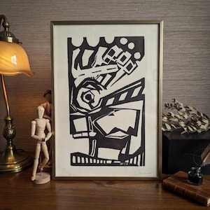 Peut inclure: Une impression linogravure abstraite en noir et blanc encadrée, présentant des formes géométriques audacieuses, des lignes angulaires nettes et une composition à fort contraste. L'œuvre est insérée dans un cadre métallique fin.