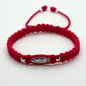 May include: Red macrame bracelet with a silver Virgin Mary charm and silver beads. The adjustable bracelet is made of a thick, woven red cord. The charm is oval-shaped and features a detailed depiction of the Virgin Mary.