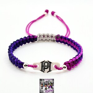 May include: A woven cord bracelet featuring a central white rectangular charm with a black HP logo. The cord is braided in alternating shades of dark purple and magenta, accented by two silver-toned beads and a light gray sliding knot closure.