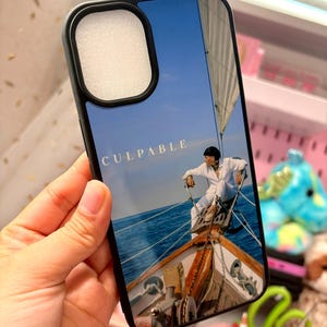 Puede incluir: Funda de teléfono negra con una imagen brillante de una persona en un velero bajo un cielo azul. La palabra "CULPABLE" está impresa en blanco en la parte superior.