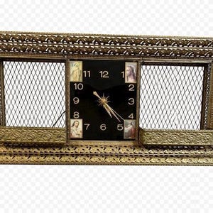 May include: An antique gold-toned wall clock with a black clock face and gold hands. The clock has a rectangular frame with decorative detailing and two openwork sections. The clock face features Roman numerals and small religious images.