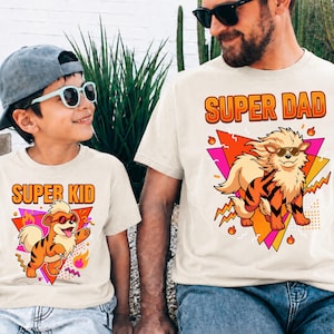 Peut inclure: Deux t-shirts cr&egrave;me assortis. L'un affiche "SUPER KID" et l'autre "SUPER DAD" en orange. Chaque t-shirt pr&eacute;sente un tigre de dessin anim&eacute; portant des lunettes de soleil et un motif g&eacute;om&eacute;trique color&eacute;. Pour un parent et son enfant.
