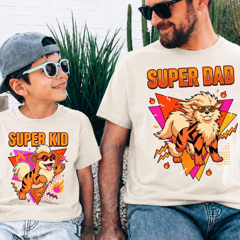 Peut inclure: Deux t-shirts cr&egrave;me assortis. L'un affiche "SUPER KID" et l'autre "SUPER DAD" en orange. Chaque t-shirt pr&eacute;sente un tigre de dessin anim&eacute; portant des lunettes de soleil et un motif g&eacute;om&eacute;trique color&eacute;. Pour un parent et son enfant.