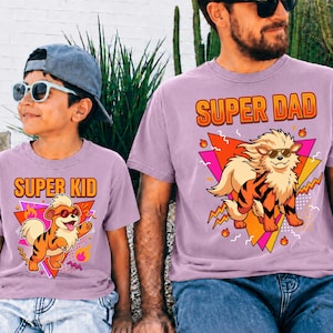Peut inclure: Deux t-shirts lilas assortis avec les inscriptions "SUPER DAD" et "SUPER KID" en orange. Chaque t-shirt pr&eacute;sente un personnage de dessin anim&eacute; avec des lunettes de soleil et un motif de tigre. Un ensemble amusant pour p&egrave;re et enfant.
