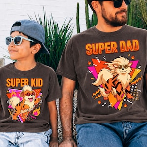 Peut inclure: Deux t-shirts bruns avec des graphiques assortis. L'un dit "SUPER PAPA" et l'autre "SUPER ENFANT". Chaque t-shirt pr&eacute;sente un chien de dessin anim&eacute; portant des lunettes de soleil, sur un fond g&eacute;om&eacute;trique color&eacute;. Les chemises sont port&eacute;es par un p&egrave;re et son enfant.