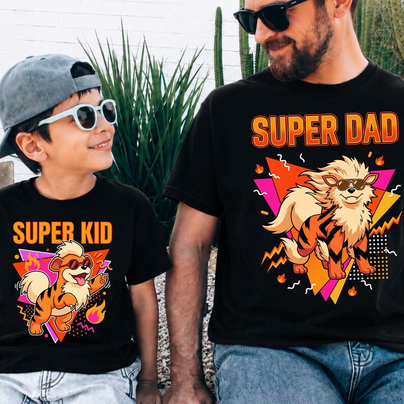 Peut inclure: T-shirts noirs avec des graphiques assortis. L'un des t-shirts affiche "SUPER PAPA" et l'autre "SUPER ENFANT". Chaque t-shirt pr&eacute;sente un chien de dessin anim&eacute; portant des lunettes de soleil, sur un fond g&eacute;om&eacute;trique avec des flammes.