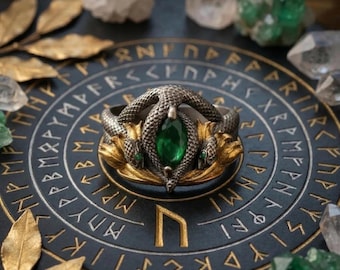 Puede incluir: Un anillo plateado con diseño de serpiente y una gran gema verde. El anillo tiene dos cabezas de serpiente a cada lado de la gema y un cuerpo de serpiente que se enrolla en la parte superior. El anillo está sobre una superficie azul oscuro con runas doradas.