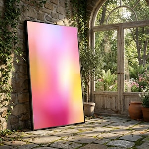 Puede incluir: Un cuadro enmarcado con un diseño abstracto y vibrante. La obra presenta un degradado de colores rosa, amarillo y naranja, dentro de un marco negro. El cuadro se apoya contra una pared de piedra, con un jardín visible al fondo.