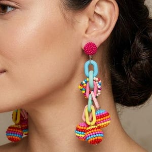 May include: Brightly coloured beaded earrings featuring a pink stud, light blue chain links, and dangling beaded spheres in rainbow shades. These earrings have a fun and lively design, ideal for adding a splash of colour to any ensemble.