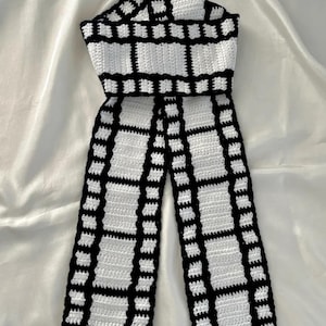 Könnte beinhalten: Handgehäkelter Schal mit auffälligem schwarz-weißem Karomuster. Der Schal ist aus weichem Garn gefertigt und hat ein einzigartiges Design, perfekt, um jedem Outfit einen Hauch von handgefertigtem Flair zu verleihen. Der Schal ist ein stilvolles Accessoire.