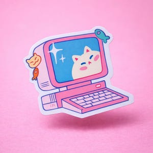 Puede incluir: Una pegatina rosa con un diseño de ordenador retro con una cara de gato en la pantalla. La pegatina tiene un teclado y está decorada con pequeñas ilustraciones de peces y gatos. El fondo es de color rosa liso.