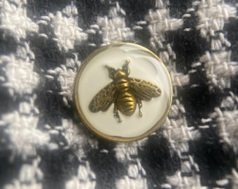 White enamel button featuring an antique gold-tone bee design.