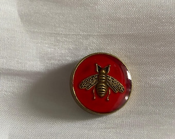 Red enamel button featuring an antique gold-tone bee design.