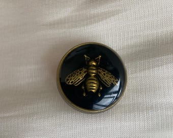 Black enamel button featuring an antique gold-tone bee design.